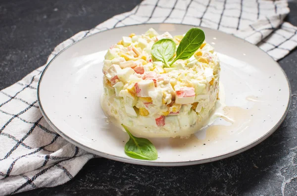 Traditional Russian salad with corn, crab meat and mayonnaise on a black stone background