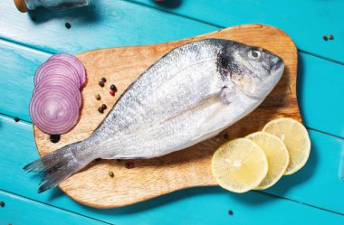 Çiğ dorado balığı, mavi ahşap masada, yemek pişirmek için gerekli malzemelerle birlikte..