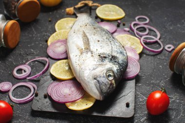Çiğ dorado balığı, siyah taş masada yemek pişirmek için gerekli malzemelerle birlikte..