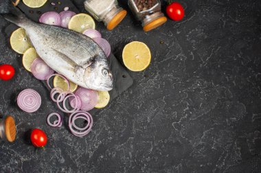 Siyah taş masada çiğ dorado balığı ve pişirmek için gerekli malzemeler. Kopyalama alanı olan üst görünüm.