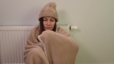 Ekoseye sarılı şapka takan genç bir kadın ısıtılmamış dairede soğuktan titreyerek tek başına oturuyor ve merkezi ısıtma borusu yok. Sağlıksız kadın rahatsızlığı evde ısınmaya çalışır.
