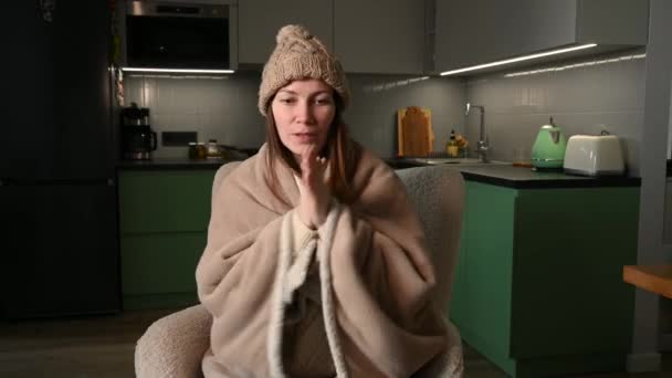 여성은 부채로 가열하지 가열되지 아파트에서 추위에서 플레이드에 모자를 착용합니다 불건강 — 비디오