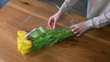 Kadın çiçekçi çiçekçide sarı lalelerden bir buket yapar. Çiçek tasarım stüdyosu, dekorasyon ve kompozisyon üretimi. Çiçek teslimatı