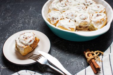 Tarçınlı rulo ya da tarçınlı, ev yapımı tatlı tarifi beyaz krema soslu ve koyu taştan arka planda..