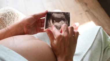 Tanımlanamayan hamile bir kadının, doğmamış bebeğinin evde otururken çekilmiş sonografi fotoğrafına yakından bakın. Hamileliğin tadını çıkaran kadın.