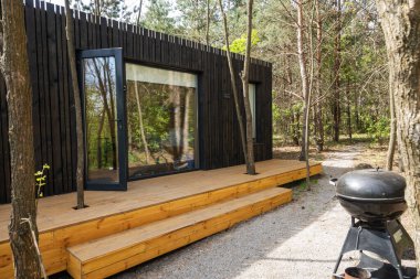 Ormandaki Ahşap Güverteli ve Izgaralı Modern Siyah Küçük Ev.