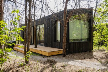 Ormandaki Ahşap Güverteli ve Izgaralı Modern Siyah Küçük Ev.