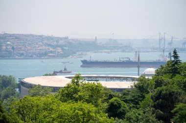 Boğaz 'dan geçen bir kargo gemisi. Maiden 's Tower ve Besiktas Stadyumu. İstanbul, Türkiye - 20 Haziran 2023.