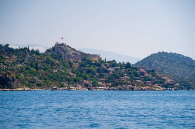 Kekova Körfezi 'nden Kalekoy kasabasının manzarası. Simena Şatosu, Türkiye 'nin çağdaş Kas kenti arasındaki Kekova Bölgesi' ndeki çarpıcı Akdeniz kıyısında yer alıyor. Antalya, Türkiye - 10 Temmuz 2023.