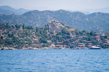 Kekova Körfezi 'nden Kalekoy kasabasının manzarası. Simena Şatosu, Türkiye 'nin çağdaş Kas kenti arasındaki Kekova Bölgesi' ndeki çarpıcı Akdeniz kıyısında yer alıyor. Antalya, Türkiye - 10 Temmuz 2023.