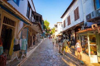 Kas 'ın eski kasabasında gün batımında butik dükkanları olan güzel bir cadde. Kas semtindeki Uzun Carsi Caddesi 'ndeki ünlü turistler. Antalya, Türkiye - 10 Temmuz 2023.