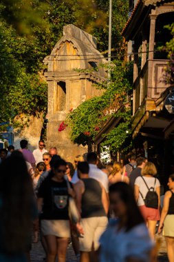 Kas 'ın eski kasabasında gün batımında butik dükkanları olan güzel bir cadde. Kas semtindeki Uzun Carsi Caddesi 'ndeki ünlü turistler. Antalya, Türkiye - 10 Temmuz 2023.