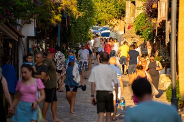 Kas 'ın eski kasabasında gün batımında butik dükkanları olan güzel bir cadde. Kas semtindeki Uzun Carsi Caddesi 'ndeki ünlü turistler. Antalya, Türkiye - 10 Temmuz 2023.