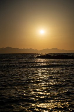 Gün batımında deniz ve ada silueti manzarası.