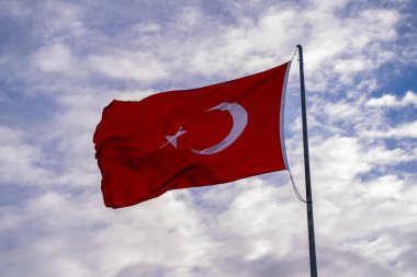 Arka planda Türk bayrağı ve bulutları sallıyor.