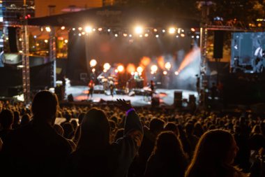 Sahne ışıkları ve insan siluetiyle dolu kalabalık bir konser salonu..