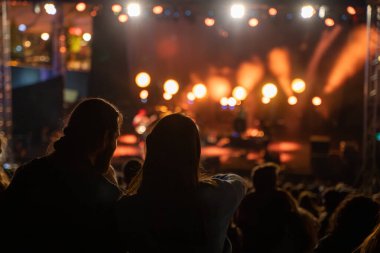 Sahne ışıkları ve insan siluetiyle dolu kalabalık bir konser salonu..