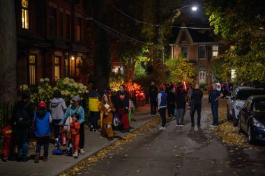 A group of children and their parents are on the street on Halloween night. Toronto, Canada - October 31, 2024. clipart