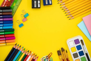Renkli okullar ve sanat malzemeleri sarı arka planda ve kopya alanı var..
