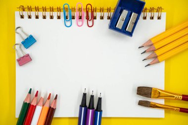 Okul düzlüğü ve sanat malzemeleri. Sarı arka planda boş defter ve kopya alanı var..