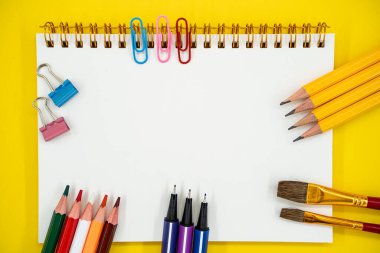 Okul düzlüğü ve sanat malzemeleri. Sarı arka planda boş defter ve kopya alanı var..