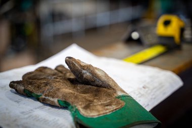 Endüstriyel bir atölyedeki teknik çizimlere dayanan kirli bir eldiveni yakından çek.