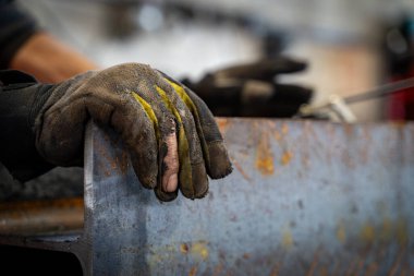 Paslı metal bir kiriş tutan yırtık eldiven giyen işçinin elini kapat..