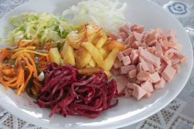 Bir tabak lahana turşusu, sarmal şekilli pancar ve havuç, kızarmış patates, yanında da jambon..