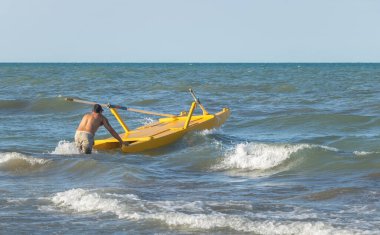 Yazın kumsalda sarı bir kano süren bir adam..