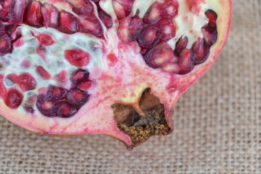 Çuval bezi arkaplanındaki açık bir narı kapat, makro fotoğrafçılık. Yarı kırmızı ve pembe narlı bir kesik tohumlar ve yumuşak beyaz posayla doludur..