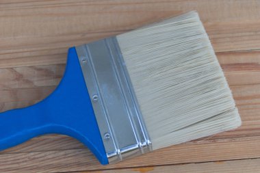 Beyaz tüylü bir boya fırçası ve ahşap bir yüzey üzerinde mavi bir sapı var..