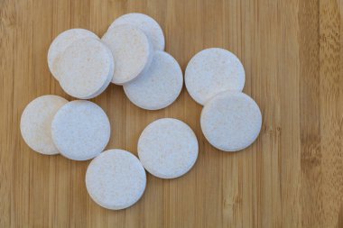 Yuvarlak beyaz haplar ahşap bir masada, yukarıdan görülüyor. Hapların yüzeyinde pürüzlü kenarlar ve küçük lekeler var.