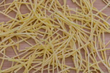 Masanın üstüne yakın plan sarı makarna eriştesi, ahşap arka planda tek sıra halinde dizilmiş ince ve uzun makarna şeritleri..