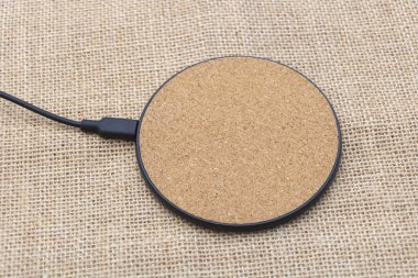 Üzerinde kablosuz kablosuz şarj portu olan dairesel bir mantar mat, bir çuval bezi arka planına karşı izole edilmiş..