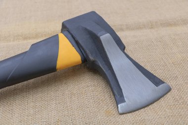 Sarı saplı siyah ve gri çelik bir balta, çuval bezi arka planda yatıyor..