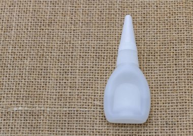 Çuval bezi arka planında beyaz plastik bir yapıştırıcı şişesi, üst manzara. Dikiş dikmek ve el işi yapmak için yapıştırıcı.