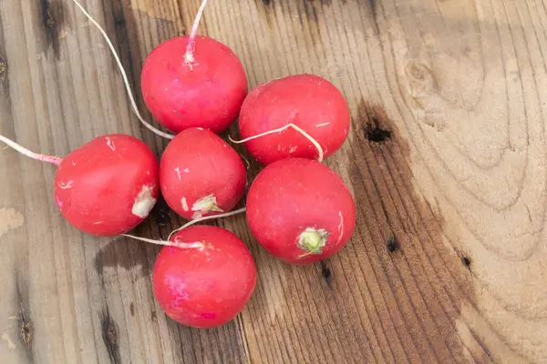 Eski ahşap bir masa üzerinde parlak kırmızı turpların yukarıdan aşağı görüntüsü, odak noktası tek bir canlı pembe turp yapısı etrafında..
