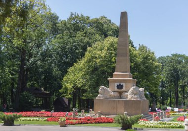 Güneşli bir günde, bir halk parkında çiçek yatakları ve gür yeşil ağaçlarla çevrili Aslan Heykelleri ve Dikilitaşlı Tarihi Anıt - Iasi, Romanya - 24 Haziran 2025