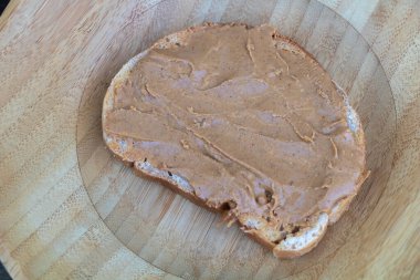 Tahta tabakta kremalı fıstık ezmeli bir dilim ekmek..