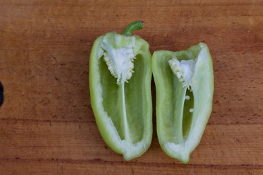 Dilimlenmiş yeşil çan biberi, kırsal bir ahşap yüzeyde tohumlar ve çukurlar ortaya çıkarıyor..