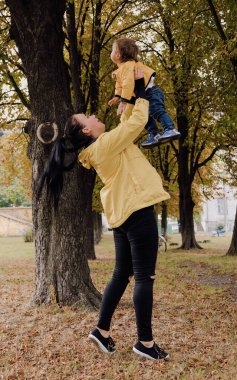 Dadı, çocuk parkında çocukla oynuyor. Anne, sonbahar havasında parkta yürüyor. Çocuklar için kaydıraklar. Çocukların gülüşü, temiz havada bir yürüyüş.
