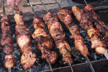 Bir adam ateşte et pişirir. Elleri yakın çekim ve şiş kebap. Izgarada domuz boynu pişirmek. Kızarmış havuç. Yağlı yiyecekler, BDT ülkelerinin şenlikli yemekleri. 1 Mayıs, İşçi Bayramı. Vejetaryen yemeği değil..