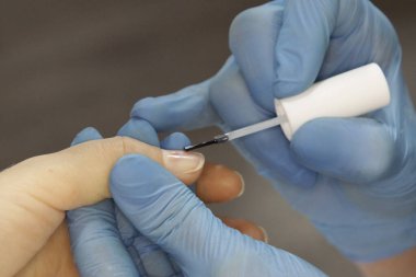 Manikür ustasının işyeri. Bir kuaför uzmanı müşterisiyle çalışır. Steril eldiven takan bir tırnak teknisyeni. El bakımı, oje başvurusu. Güzellik salonu manikürü ve pedikür..