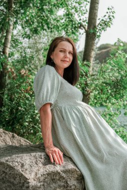 Nehir kıyısında hamile bir kız. Bir çocuğun doğmasını bekliyorum. Elinde sazlıktan yapılmış çiçek buketi olan bir kadın. Köylü bir kız suyun kenarında oturuyor..