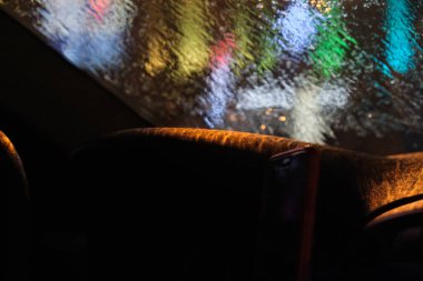 Heavy rain behind the windshield of a car. Blurred image from bad weather. Dashboard. Glare of multi-colored ones outside the window.Misted car window from strong moisture.