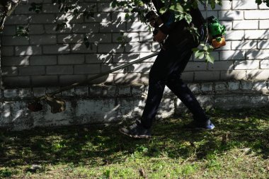 Cleaning the area from grass and weeds. Smooth lawn outside. Man cleaning a public street with a manual lawn mower
