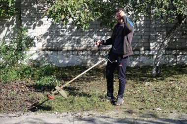 Cleaning the area from grass and weeds. Smooth lawn outside. Man cleaning a public street with a manual lawn mower