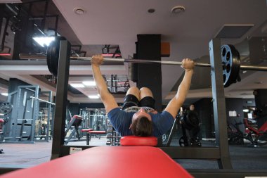 February 21, 2023 Ukraine, Dnipro.Barbell bench press. A young athlete on a simulator in a supine position loads the muscles of his arms and chest. Training of muscle groups of the upper body. gym