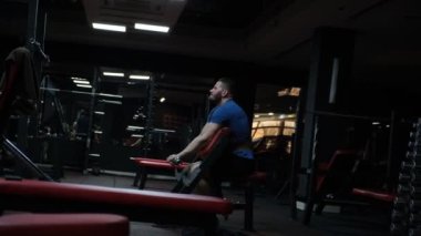 Otururken halterle egzersiz yapan güçlü bir vücut geliştirici. Sporcu fitness adamı kol kaslarını şişiriyor, vücut geliştirme egzersizi, arka plan konsepti - kaslı yakışıklı erkekler jide spor yapıyor.