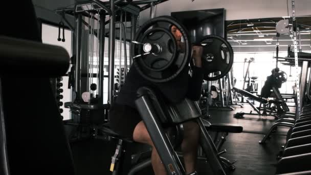 按下杠铃 一个年轻的运动员在模拟器上做仰卧起坐的姿势 他的胳膊和胸部的肌肉负荷着 训练上身肌肉群 体育馆 — 图库视频影像
